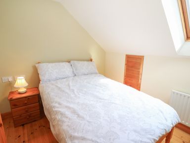 A bedroom with a double bed nightstand with a lamp wooden floor and a skylight window at Dooneen near Castletownshend County Cork