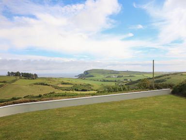 A grassy lawn with a low wall overlooking green fields hills and a partly cloudy sky at Dooneen near Castletownshend County Cork