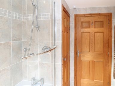 A bathroom with a corner shower and two wooden doors at Bryn Eiddon in Aberdaron