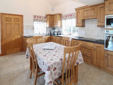 A kitchen with wooden cabinets and a table with a heart patterned tablecloth at Bryn Eiddon in Aberdaron