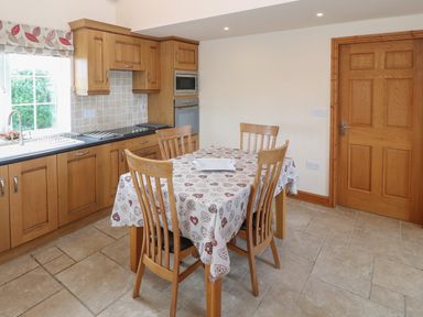 A kitchen with wooden cabinets a table with four chairs and a tiled floor at Bryn Eiddon in Aberdaron