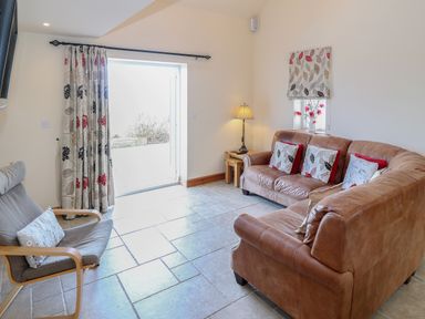 A sitting room with two leather sofas a wooden chair with cushion and a lamp at Bryn Eiddon in Aberdaron