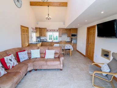 A kitchen and living room with a brown leather corner sofa and a grey armchair at Bryn Eiddon in Aberdaron