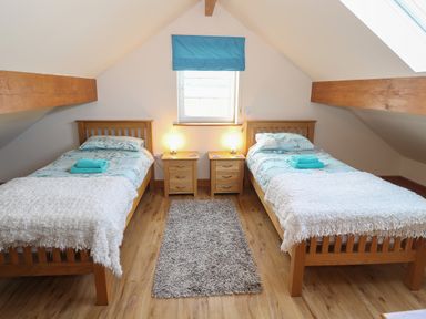 A bedroom with two single wooden beds two bedside tables with lamps and a window with a blue blind at Bryn Eiddon in Aberdaron