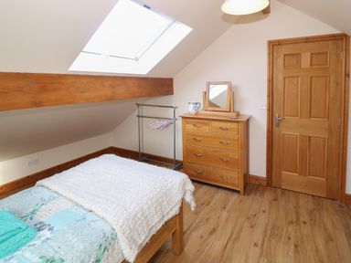 A bedroom with a bed covered with a white blanket a wooden dresser with a mirror a clothes rack with hangers and a wooden door at Bryn Eiddon in Aberdaron