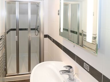 A bathroom with a glass shower enclosure a white sink with a chrome faucet a mirror and a heated towel rail at Bryn Eiddon in Aberdaron