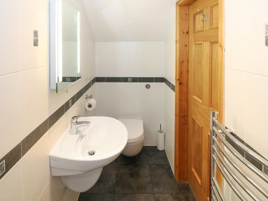 A small bathroom with a wall-mounted sink toilet wooden door and heated towel rail at Bryn Eiddon in Aberdaron