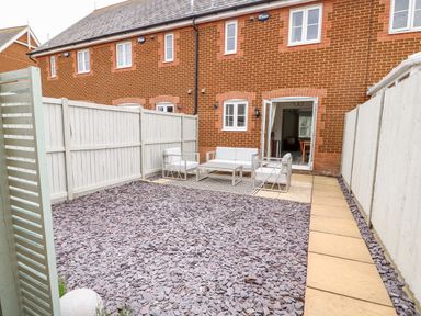 An outdoor patio with stone flooring chairs a table and a white fence at 5 Styleman Road Hunstanton