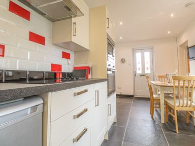 A kitchen with white cabinets red and white tiled backsplash and a dining table with chairs at Y Bwthyn Newport in Newport Pembrokeshire