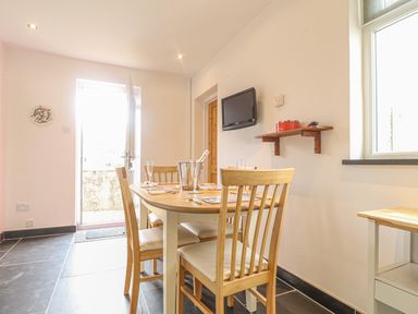 A dining area with a wooden table and chairs a wall-mounted TV and a door leading outside at Y Bwthyn Newport in Newport Pembrokeshire