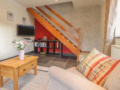 A living room with a wooden coffee table flowers on the table a sofa with a striped cushion television on the wall and wooden stairs at Y Bwthyn Newport