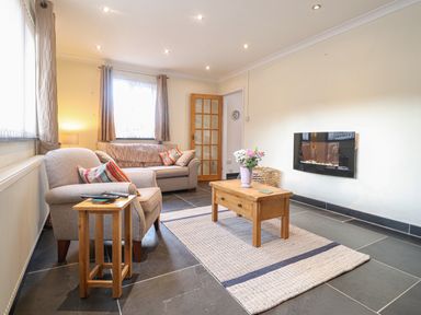 A living room with two armchairs a coffee table and a wall-mounted electric fireplace at Y Bwthyn Newport