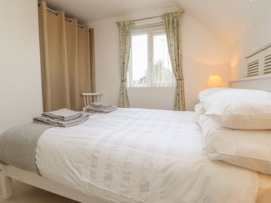 A bedroom with a bed with white bedding folded towels on the bed and a window with curtains at Y Bwthyn Newport in Newport Pembrokeshire
