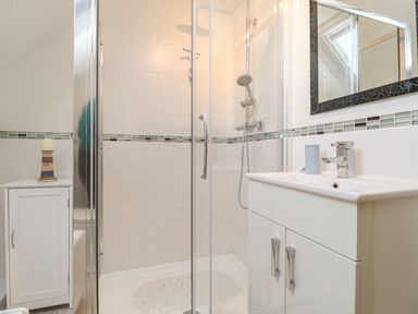 A bathroom with a shower enclosure a sink with a cabinet and a small cabinet with a candle on top at Y Bwthyn Newport in Newport Pembrokeshire
