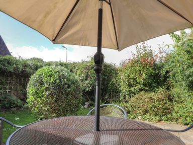 An outdoor patio table with an umbrella in a garden with bushes and a hedge at Y Bwthyn Newport