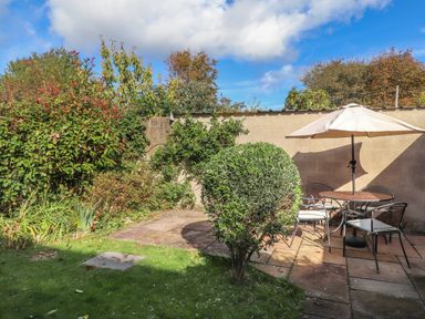 A garden area with green grass a small tree a round table with chairs and an umbrella at Y Bwthyn Newport
