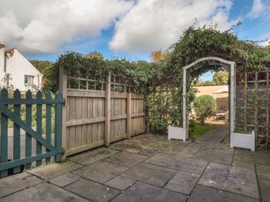 A garden area with a wooden gate and an archway covered in vines leading to a patio with a table and chairs at Y Bwthyn Newport in Newport Pembrokeshire
