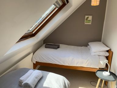 A bedroom with two single beds a skylight window a bedside table with a lamp and towels on the beds at Y Bwthyn Newport Pembrokeshire