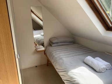A small bedroom with a single bed near a slanted window and a mirror on the wall at Y Bwthyn Newport in Newport Pembrokeshire