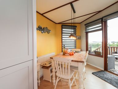 A dining area with a wooden table and white chairs next to large windows and a sliding door at 4 Country View Park in Graveney near Seasalter