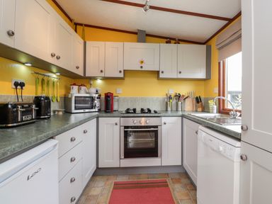 A kitchen with white cabinets, a gas stove, microwave, toaster, coffee machine, sink, and utensils at 4 Country View Park in Graveney near Seasalter
