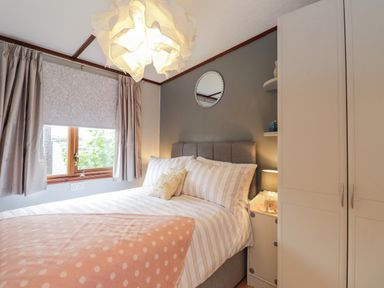 A bedroom with a bed under a window beside a wardrobe and bedside table at 4 Country View Park in Graveney near Seasalter