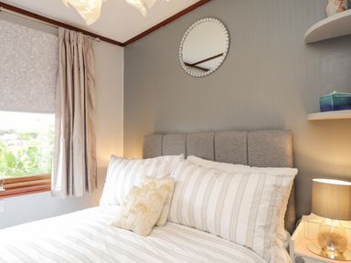 A bedroom with a bed with striped pillows and a grey headboard a lamp on a bedside table and a round mirror on the wall at 4 Country View Park in Graveney near Seasalter