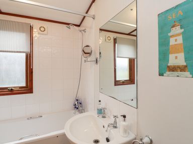 A bathroom with a bathtub shower combination sink and a mirror with a lighthouse wall decoration at 4 Country View Park in Graveney near Seasalter
