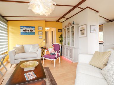 A living room with white sofas a purple chair a wooden coffee table a glass cabinet and yellow walls at 4 Country View Park in Graveney near Seasalter