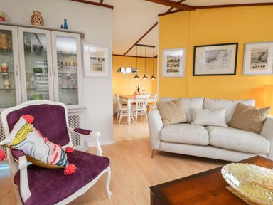A living room with a beige sofa and purple armchair next to a glass cabinet and a dining area visible beyond at 4 Country View Park in Graveney near Seasalter