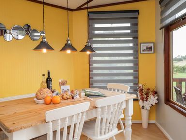 A dining area with a wooden table set with bread oranges wine and other items three hanging lights and white chairs at 4 Country View Park Graveney near Seasalter