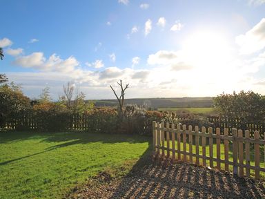 A garden with a wooden picket fence overlooking fields under a blue sky at Valley View in Mevagissey