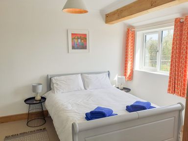 A bedroom with a double bed white bedding blue towels bedside tables and orange curtains at Valley View in Mevagissey