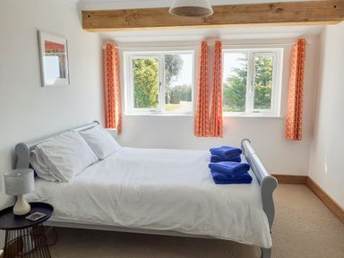 A bedroom with a double bed white bedding blue towels on bed orange curtains and a window at Valley View Mevagissey