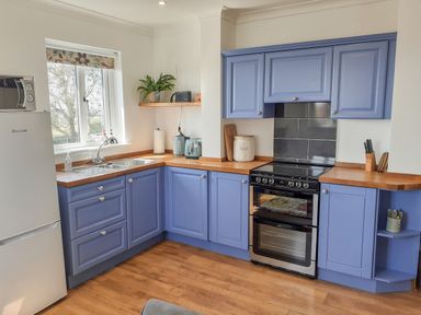 A kitchen with blue cabinets wooden countertops and a window at Valley View in Mevagissey