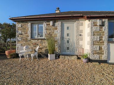 A stone cottage exterior with a gray door and windows a small white table and chairs and potted plants at Valley View in Mevagissey