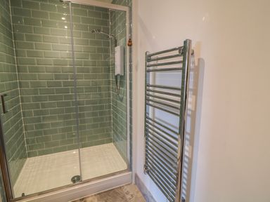 A bathroom shower area with green tiled walls and a glass door next to a chrome heated towel rail at Valley View in Mevagissey