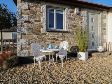 An outdoor stone patio with a white metal table and two chairs with a blue teapot set in front of a stone wall at Valley View in Mevagissey