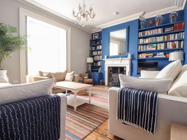 A living room with beige sofas striped blankets a wooden coffee table a chandelier and blue built in bookshelves at The Water House in Falmouth