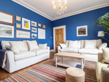 A living room with two white sofas a wooden coffee table a striped rug and blue walls with framed pictures at The Water House in Falmouth