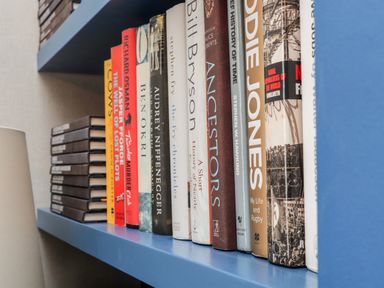 A blue bookshelf with various books and stacked black notebooks at The Water House in Falmouth