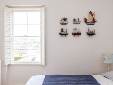 A bedroom with a window with shutters model boats on the wall and a bed with a blue blanket at The Water House in Falmouth
