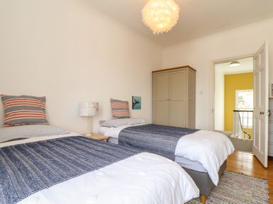 A bedroom with two single beds a striped pillow a lamp a wardrobe and an open door showing a hallway at The Water House in Falmouth