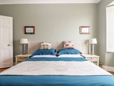 A bedroom with a bed with blue bedding and two patterned cushions two bedside tables with lamps and framed pictures on the wall at The Water House in Falmouth