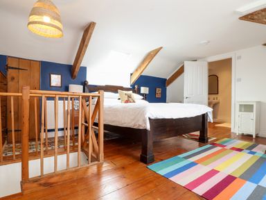 A bedroom with a wooden bed and white bedding a colorful striped rug and wooden floor at The Water House in Falmouth