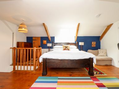 A bedroom with a wooden bed white bedding a colorful rug and wooden furniture at The Water House in Falmouth