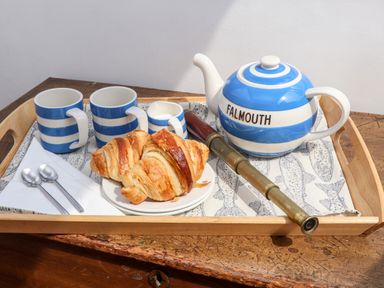 A wooden tray with blue and white striped teapot and mugs croissants spoons and a brass telescope on a wooden table at The Water House in Falmouth