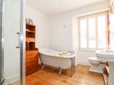 A bathroom with a clawfoot bathtub wooden cabinet toilet sink and a window with shutters at The Water House in Falmouth