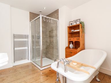 A bathroom with a freestanding bathtub shower enclosure wooden floor and a wooden cabinet at The Water House in Falmouth
