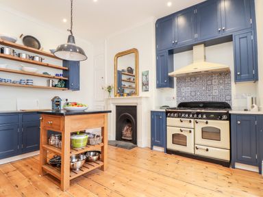 A kitchen with blue cabinets wooden island and a stove with tiled backsplash at The Water House in Falmouth